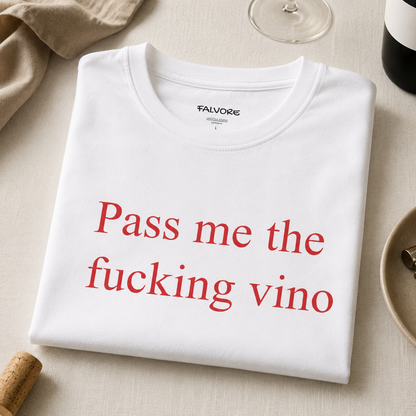 White t-shirt with red text 'Pass me the fucking vino' on a beige surface with wine-related items.
