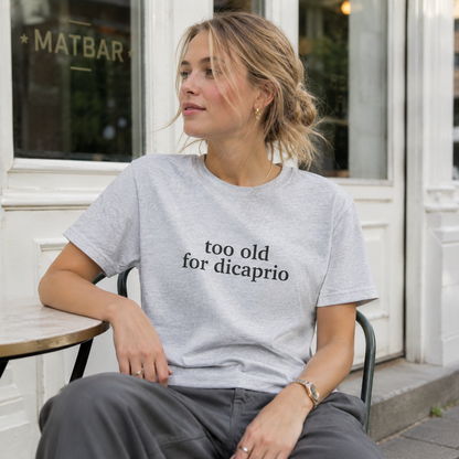Woman wearing a t-shirt with 'too old for dicaprio' text sitting outside a building.